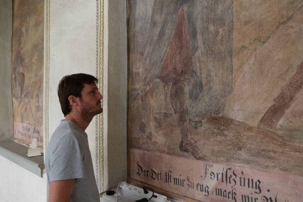 Musterrestaurierung Gemäldezyklus Hallenumgang, Klosteranlage Werthenstein LU. Florian Nick während der Arbeit an dem Gemälde Nr. 48, «Zwei Luzerner Ratsherren beraten mit einem Franziskaner den Klosterbau».