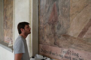 Musterrestaurierung Gemäldezyklus Hallenumgang, Klosteranlage Werthenstein LU. Florian Nick während der Arbeit an dem Gemälde Nr. 48, «Zwei Luzerner Ratsherren beraten mit einem Franziskaner den Klosterbau».