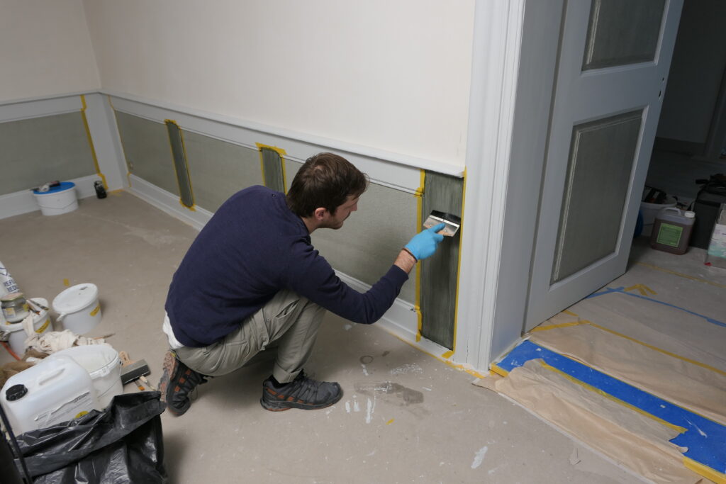 Rekonstruktion Dekorationsmalerei, Wohnhaus Sternenweg 9, Baar ZG. Der Restaurator fügt der aufgebrachten Ölfarbe mittels eines Borstenpinsel eine wellige Struktur zu.